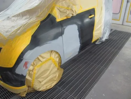 これから塗装工程に入りますが車を塗装専用ブースに移動して塗料がかかってはまずい部分を専用のシートでマスキングを行います。<br>塗装はまず、サフェーサを塗布するところから始まります。<br>サフェーサとは塗料の下地となる塗料のことです。<br>板金仕上げに使うパテが塗料を吸い込まないようにしっかりシールし、塗装面を滑らかにします。<br>塗装面を溶剤できれいに脱脂した後、サフェーサを塗布し、赤外線ヒーターで十分に加熱乾燥を行います。