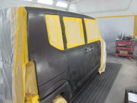 新しいドアが入庫して、建付けを確認しながら取り付けて行きました。<br>新品のドアは非常に高い防錆力を持つ電着塗装が施された状態で供給されます。<br>(殆どの場合黒い塗装膜)なので、現車の色に合わせて塗装をすることとなります。<br>塗装は専用のブース(密閉した部屋)にて塗装中のホコリの付着などを防ぎます。<br>さらに塗装中の塗料の飛散による汚れを防止するために、塗装面以外は全て専用のビニールシートやペーパーでマスキングを行ってから塗装を開始します。<br>塗装前の準備として、細かいサンドペーパー研磨する足付けを行います。<br>次に塗装面の脂分・ワックス分を専用の溶剤で落とす脱脂の作業を行います。<br>今回の塗装はリアドアに隣接するクオーターパネル及びフロントドアのぼかし塗装も含めて行う事になります。<br>まず、塗装色を現車の色に合わせて作っていきますが、調色は専門の塗装職人が数種類のサンプルを作成して、車に直あてして、最も現車の色に近い色をベースカラーとして決めます。<br>ベースカラーが決定すると塗料を専用のスプレーガンで数回に分けて吹き付けていきます。