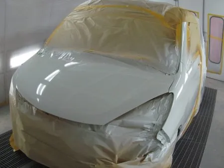 次の工程として塗装面の脂分・ワックス分を専用の溶剤で落とす脱脂の作業を行います。<br>今回の塗装は取り換えられたバンパーとフェンダー以外に隣接するフロントドアとボンネットフードのぼかし塗装も含めて行う事になります。<br>バンパーは別に単体で塗装を行います。<br>まず、塗装色を現車の色に合わせて作っていきますが、調色は専門の塗装職人が数種類のサンプルを作成して、最も現車の色に近い色をベースカラーとして決めます。<br>ベースカラーが決定すると塗料を専用のスプレーガンで数回に分けて吹き付けていきます。<br>その次に透明なクリア塗装をします。<br>トップコートとしてのクリア塗装をすることで、紫外線による塗料の劣化防止及び対候性を高めることが出来ます。